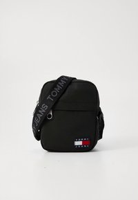 Compatta borsa a tracolla nera con tasca frontale con cerniera, patch con logo Tommy Jeans e tracolla regolabile con marchio.
