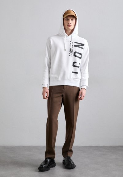 Weißer Kapuzenpullover mit schwarzem vertikalem Text, kombiniert mit braunen maßgeschneiderten Hosen und schwarzen Schnürschuhen. Einfaches Design, lässiger Stil.