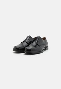 Chaussures habillées en cuir noir avec une finition brillante, bout arrondi, design à lacets et construction minimaliste. Talon bas en caoutchouc solide.