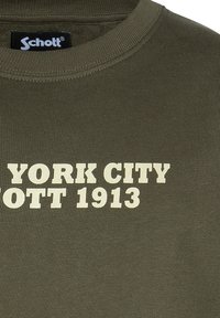 T-shirt verde oliva scuro in cotone, con bold testo bianco che recita “NEW YORK CITY” e “SCHOTT 1913” in un font classico.