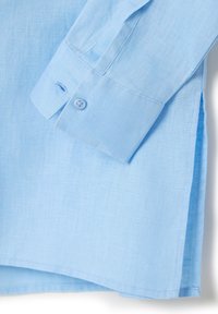 Himmelblaues Leinenhemd mit geknöpften Manschetten und seitlichen Schlitzen, aus strukturiertem Stoff mit sauber genähten Säumen.