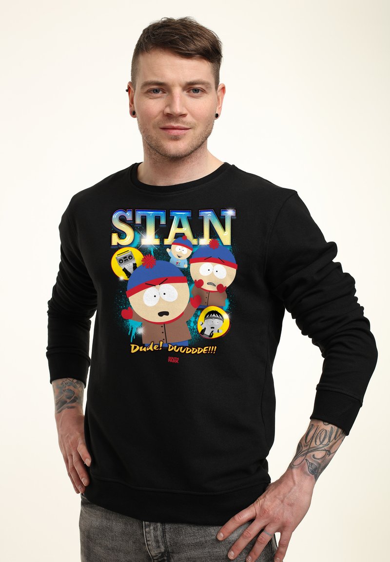 Homme portant un sweat-shirt noir avec le personnage animé Stan de South Park, avec un texte coloré et des graphismes sur le devant.