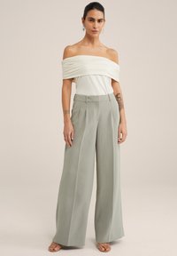 Top crema scollato con dettagli arricciati abbinato a pantaloni a gamba larga a vita alta in tessuto verde chiaro. Texture liscia, design minimalista.