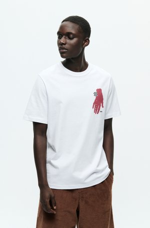 White cotton t-shirt with a graphic of a red hand and checkered accents on the upper left chest. Relaxed fit, crew neckline.