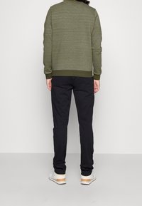 Felpa grigia oliva testurizzata con scollo rotondo, abbinata a pantaloni neri a sigaretta e sneakers chiare con dettagli in legno.