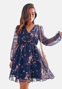 Navy bloemenjurk van doorzichtige stof, met een wikkelontwerp, lange mouwen en een elastische taille, met roze en witte bloemenpatronen.