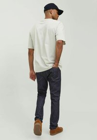 Camiseta gris de manga corta, jeans azul oscuro y zapatos de ante beige. Los detalles notables incluyen bolsillos, costuras y un corte relajado.