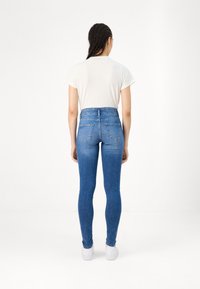Jeans de tiro alto de color azul con una silueta ajustada, que cuentan con bolsillos traseros y una textura de denim suave, combinados con una camiseta blanca.