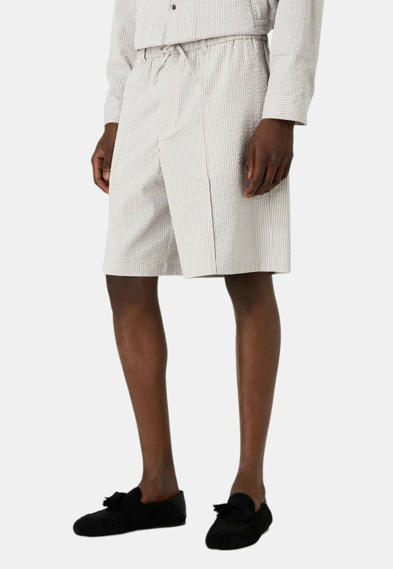 Pantaloni corti a righe grigio chiaro realizzati in tessuto testurizzato, con elastico in vita e vestibilità comoda. Presentano una spaccatura laterale per maggiore facilità.