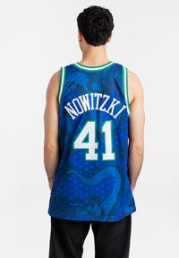 Camiseta de baloncesto azul con un patrón de dragón, con el nombre "NOWITZKI" y el número "#41" en la parte posterior, y con un ribete a rayas verdes y blancas.