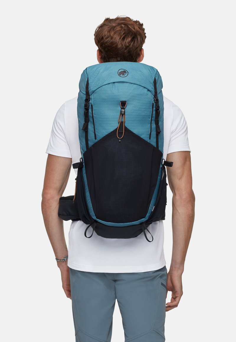 Ryggsäck i teal och svart tyg med rutmönster, övre klaffstängning, dragsnodd, sidostöd och vadderat ryggstöd.