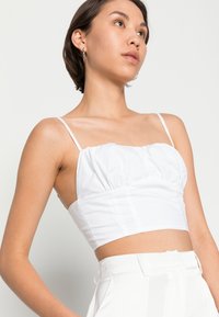 Top branco cropped com alças finas, textura franzida na zona do busto e corpete justo. Usado com calças brancas de cintura alta.