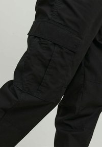 Pantaloni cargo neri con una texture liscia, dotati di ampie tasche laterali e un design aderente in vita, che enfatizza funzionalità e utilità.