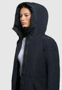 Sort hættetrøje lavet af glat stof, med lynlåslukning, stor hætte og sidelommer med minimalistiske design detaljer.