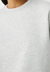 Light gray sweatshirt made of soft fabric with a textured surface, featuring a classic crew neckline and ribbed detailing at the collar.