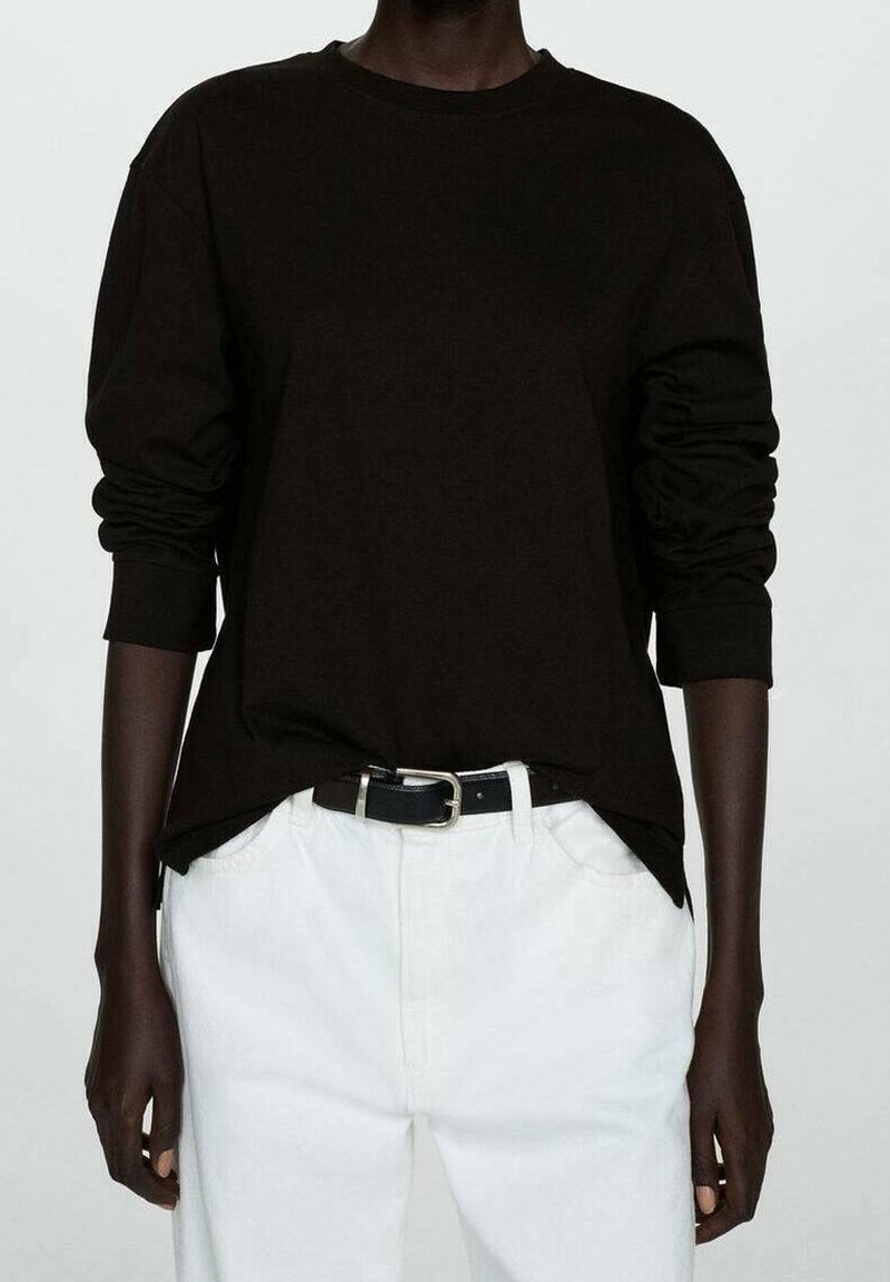T-shirt noir à manches longues avec col rond, en tissu doux, associé à un pantalon blanc taille haute et une ceinture noire.