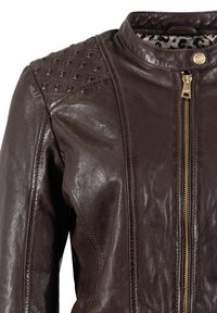 Braune Lederjacke mit hohem Kragen, schrägen Nähten, Reißverschlüssen und Schulterakzenten im Rautenmuster. Gefüttert mit einem Stoff im Leopardenmuster.
