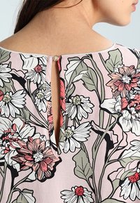 Floral blouse featuring a light pink fabric with black outlines. Round neckline, keyhole back with a small round button detail.