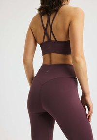 Lila Sport-Crop-Top mit einem trägerlosen Design und passenden hochgeschnittenen Leggings. Glatte Textur, figurbetonte Silhouette und Logodetail.