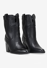 Botines de cuero negro hasta el tobillo con punta redonda, costuras laterales verticales, detalles recortados y un tacón cuadrado apilado. Textura suave.