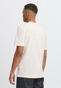 Camiseta de manga corta en color crema, hecha de una tela suave, con un corte clásico, dobladillo recto y un diseño minimalista.