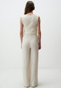 Weißer, strukturierten Jumpsuit mit tailliertem Oberteil, weiter Hose und einem gitterartigen Muster. Ärmeloses Design mit rundem Ausschnitt.