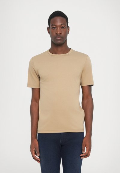 Beige kortermet T-skjorte laget av bomullsblanding, med rund hals, glatt tekstur og en kroppsnær silhuett, sammen med mørkeblå jeans.