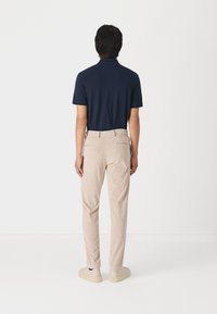 Marineblå polo-shirt med korte ærmer, parret med lysebeige teksturerede bukser og beige sko, set fra ryggen.