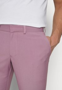 Lila hlače uskog kroja, izrađene od glatkog materijala. Imaju ravni prednji dio, bočne džepove i elegantan pojas.