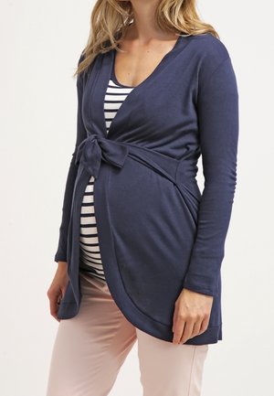 Marineblauwe zwangerschapscardigan met een strik in de taille, lange mouwen en een diepe V-hals, gedragen over een marineblauw en wit gestreept shirt.