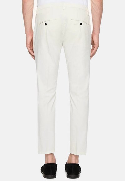 Pantaloni bianchi su misura con una vestibilità slim, tasche posteriori con bottoni neri e una texture liscia, abbinati a scarpe nere.