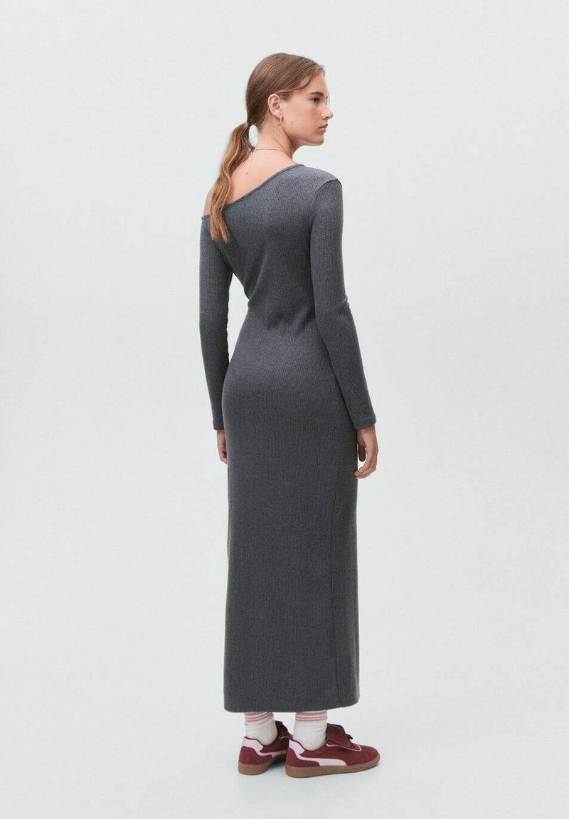 Abito grigio a maniche lunghe a coste con scollatura off-shoulder. Silhouette aderente con gonna dritta fino alla caviglia. Indossato con sneakers rosse e calze bianche.