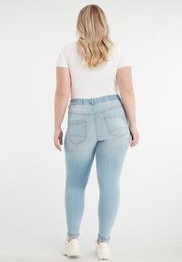 Jasnoniebieskie dżinsy jeggings z elastycznym paskiem w talii, z dwoma tylnymi kieszeniami i gładką strukturą. Połączone z białą koszulką i sportowymi butami.