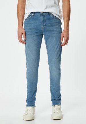 Jasnoniebieskie jeansy slim-fit wykonane z denimu, z pięcioma kieszeniami, gładką teksturą i zapięciem na guzik w talii. Połączone z białymi trampkami.