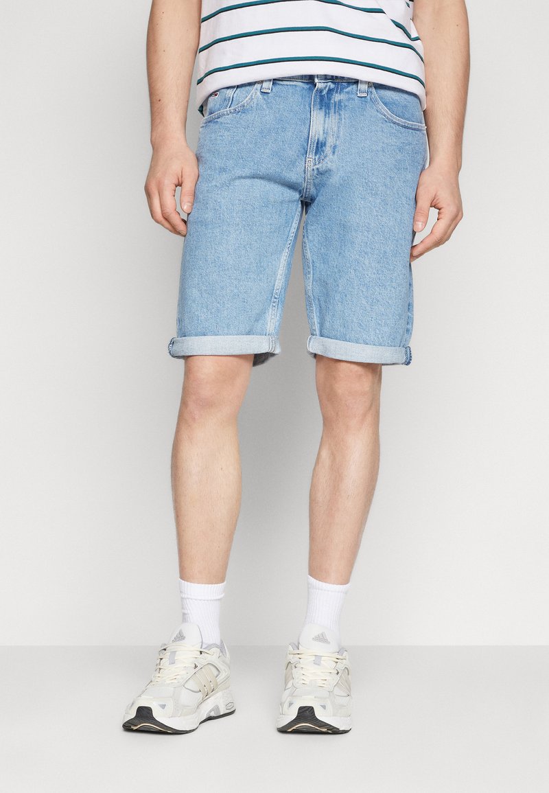 Pantalones cortos de mezclilla azul claro con dobladillos enrollados, que cuentan con un diseño clásico de cinco bolsillos. Llevados con una camisa a rayas y zapatillas deportivas blancas.