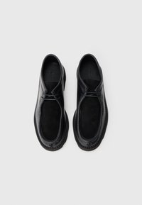 Schwarze Lederschuhe mit abgerundetem Zehenbereich, glatter Oberfläche, strukturiertem Wildlederpaneel und gesteppten Akzenten. Sicherer Schnürverschluss, flaches Design.