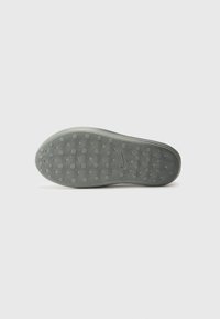 Shoe sole featuring textured gray rubber with circular and dotted patterns for grip. Smooth edges and rounded shape.