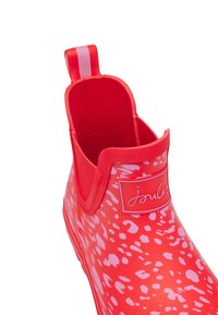 Botte de pluie en caoutchouc à motif rouge et rose avec doublure en tissu et languette de traction à l'arrière, avec une étiquette de marque "Joules" à l'avant.