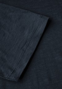 Tmavě námořnické tričko s krátkým rukávem, které se vyznačuje hladkou texturou a jemným leskem. Okraje lemu a rukávů jsou prošity, což ukazuje na pečlivé zpracování.