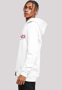 Fehér kapucnis sweatshirt elülső zsebből, állítható húzózsinórral a kapucnin és piros logó szöveggel. Bordázott mandzsettákkal és szegéllyel, sima szövettextúrával rendelkezik.