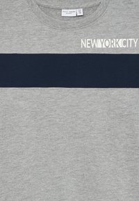 Šedá mikina s horizontálnym námorníckym pruhom a nápisom "NEW YORK CITY" v bielej farbe na hornej pravej strane. Mäkká textúra, okrúhly výstrih.