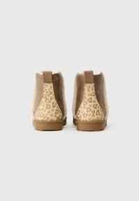 Botas de tornozelo castanhas com um exterior suave e felpudo, laterais em tom bege com um padrão de corações e uma sola de borracha texturizada.