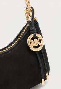 Μαύρο σουέντ τσάντα χειρός με χρυστό φερμουάρ, κυκλικό μενταγιόν με το λογότυπο MK και μαύρα δερμάτινα λουριά διακόσμησης. Λείο υλικό και δομημένο σχήμα.