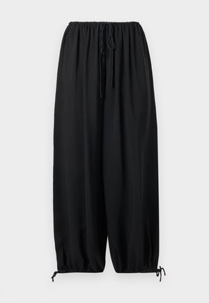 Lockere schwarze Hose mit elastischem Bund und Kordelzügen an Taille und Knöcheln vor einfarbigem Hintergrund.