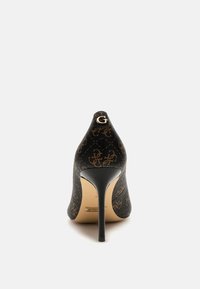 Scarpa con tacco alto in tessuto nero con motivo logo dorato, design a punta e sottile tacco a stiletto. Leggera texture sul materiale.