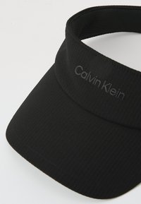 Svart visor keps tillverkad av texturerad tyg. Har en böjd skärm och ett märkt band med "Calvin Klein" i subtila bokstäver.