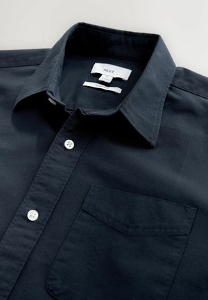 Marineblå slim fit skjorte lavet af glat stof, der har en spids krave, hvide knapper og en enkelt brystlomme. Mærket er synligt indeni.
