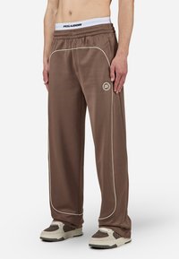 Pantalons de survêtement marron avec des passepoils blancs, taille élastique et détail de logo. Fabriqués en matériau léger et lisse. Présentent une coupe décontractée.