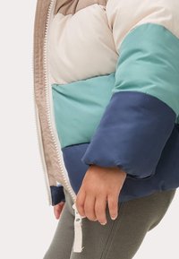 Gewatteerde jas met ritssluiting, met kleurvlakken in crème, blauwgroen en marineblauw. Zachte textuur met zichtbare stiksels en licht opgeblazen mouwen.