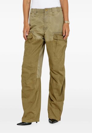 Donna che indossa pantaloni cargo bicolore oliva con più tasche, tacchi neri appuntiti e una maglietta bianca, mostrata dalla vita ai piedi.